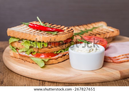 Classic club sandwich with bacon and vegetables on wooden chopping board