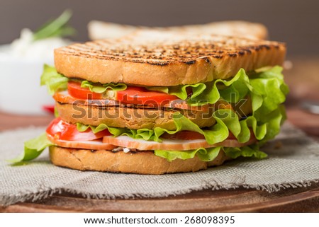 Classic club sandwich with bacon and vegetables on wooden chopping board