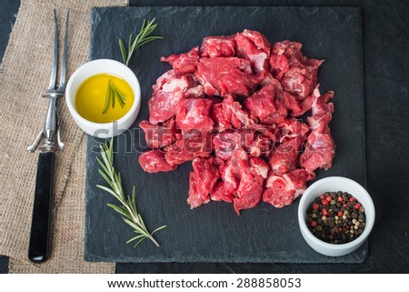 Raw beef cubes with rosemary and beefsteak spices on black background