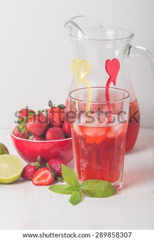 Strawberry lemonade with ice in glass on white wooden background