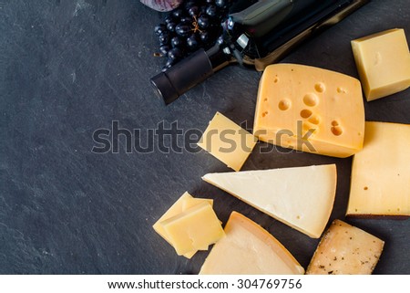 Different types of cheeses, red wine, grapes and figs on black board, top view