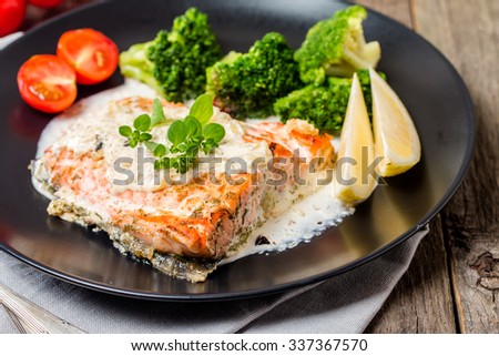 Grilled Salmon Steak with Broccoli, Cream sauce and Lemon Wedges on wooden background, close up