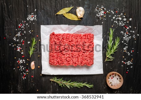 Minced meat on paper with seasoning and fresh rosemary on black background, top view
