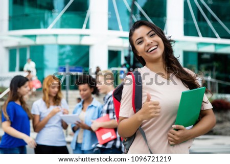Successful latin american female student showing thumb up outdoor on campus of university