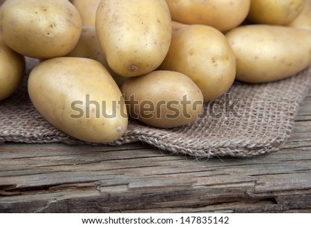 Fresh Potatoes lying on a bag on old wood