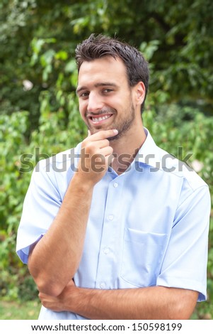 Laughing latin man in the park with green trees in the background