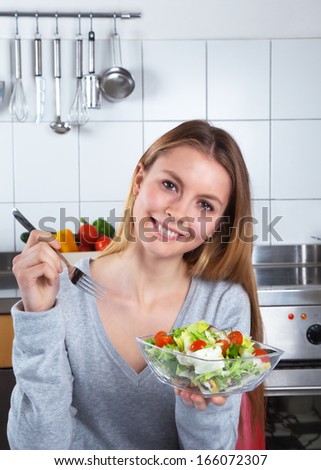 Laughing young woman at kitchen with fresh salad