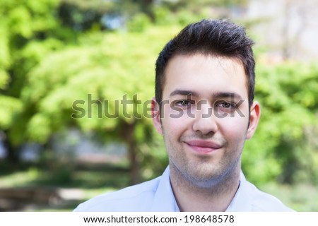 Smiling hispanic guy in a blue shirt outside in a park