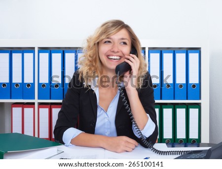 Happy blond businesswoman at office at phone