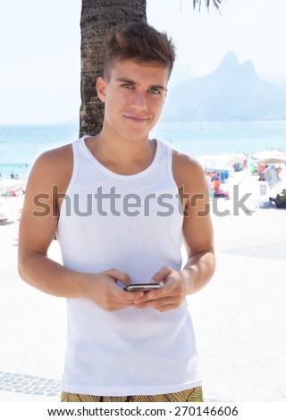 Young guy dialing with phone at beach