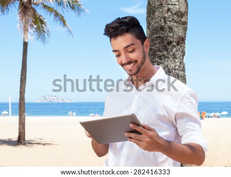 Laughing brazilian guy reading e book with tablet at beach
