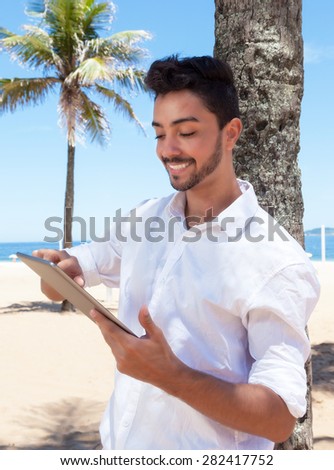 Happy brazilian guy reading e book with tablet at beach