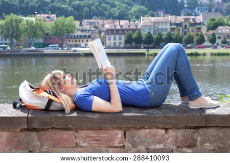 Woman with blonde hair reading a book on a river