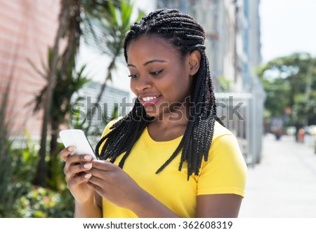 African american woman in a yellow shirt texting message with mobile phone