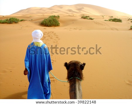 Traditional arab man walking through the desert with a camel
