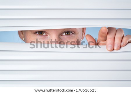 Privacy or spying concept - a young woman opening closed shutters and peeking through them.