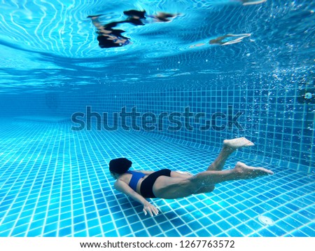 Woman swimming underwater or diving in the swimming pool, as background. Summer or sports concept.