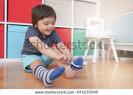 Cute little kid sitting next to tablet and learning how to put the socks on by him self, Happy Toddler boy pulling his socks to his knee , Child development concept
