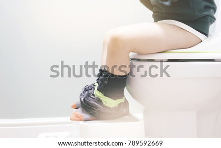 Kid sitting on toilet, Low view on his legs hanging with black jean with fluffy sock in retro tone, copy space, Training child or Health care concept.