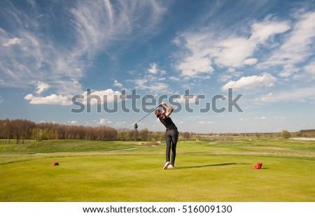 Woman golf player teeing off ball, view from behind.