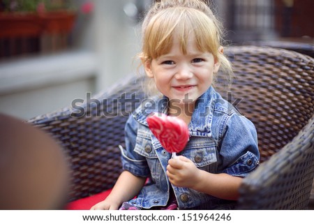 cute little girl holding a big heart shaped lollipop in the cafe outdoors