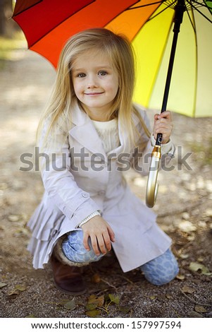 beautiful little girl with a rainbow umbrella in the autumn park