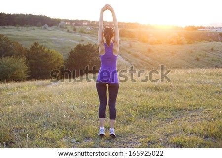 Happy successful sportswoman raising arms to the sky on golden back lighting sunset summer.