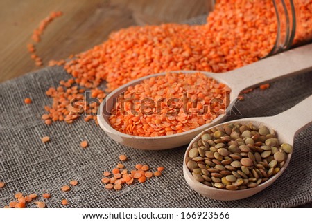 Whole green and refined red lentils in wooden spoon and glass jar on linen sackcloth