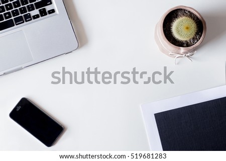 White office desk table with laptop, smartphone, cactus, and glass. Top view with copy space, flat lay.