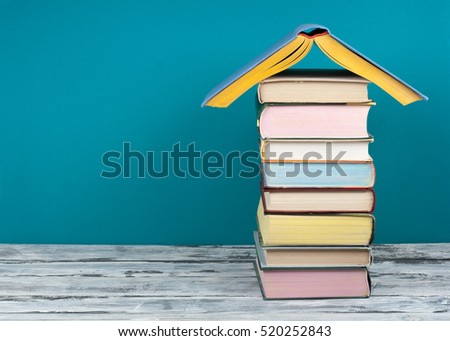 Book stacking. Open book, hardback books on wooden table and blue background. Back to school. Real estate concept, house shape. Copy space for text.