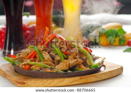 original fajita sizzling smoking hot served on iron plate ,with selection of beer and fresh vegetables on background