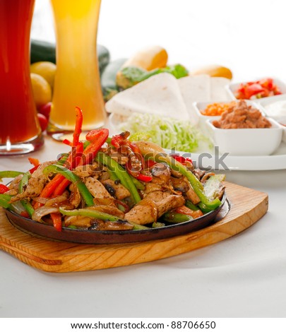original fajita sizzling smoking hot served on iron plate ,with selection of beer and fresh vegetables on background