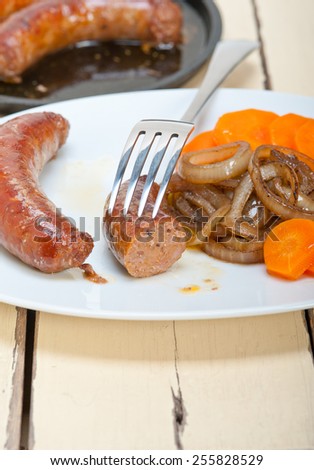 beef sausages cooked on iron skillet with carrot and onion