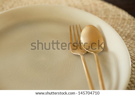 Simple design of gold spoon and fork on dish.