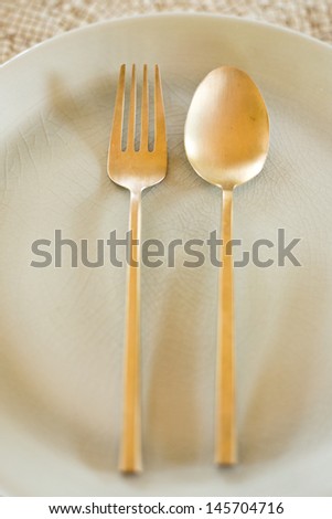 Simple design of gold spoon and fork on dish.