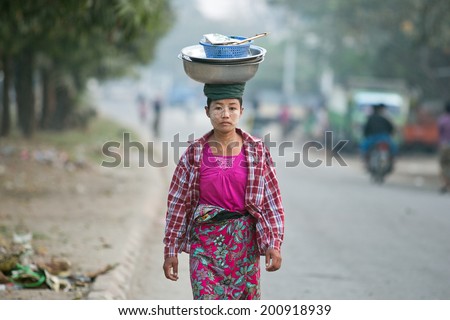 MANDALAY, MYANMAR - FEBRUARY 27 : Unidentified Burmese woman carrying enameled basin on her head on February 27, 2014 in Mandalay, Myanmar. Carrying things on head is general skill of Burmese women.
