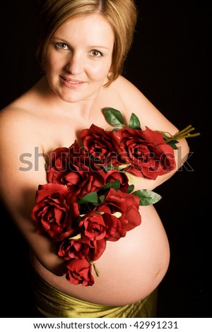 Beautiful young pregnant Caucasian woman holding flowers to cover her breasts, showing belly