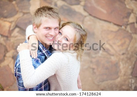 Young in-love adult couple smiling while hugging each other and looking at the viewer