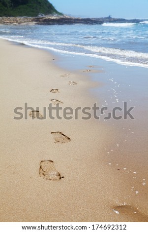 Human footprints on the beach sand with sea in background leading towards the viewer