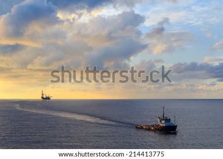 Offshore jack up drilling rig and supply boat in the middle of the ocean during sunset time