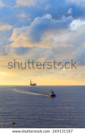 Offshore jack up drilling rig and supply boat in the middle of the ocean during sunset time