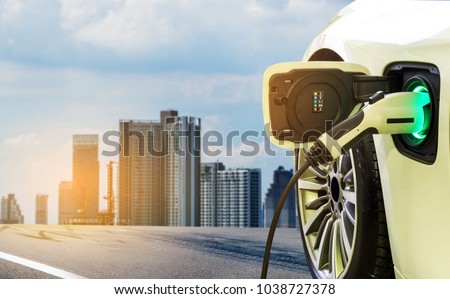 Charging modern electric car on the street with blurred building city on background. \
Eco-friendly alternative energy concept.