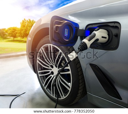 EV Car or Electric car at charging station with the power cable supply plugged in on blurred nature with sun light background. Eco-friendly alternative energy concept