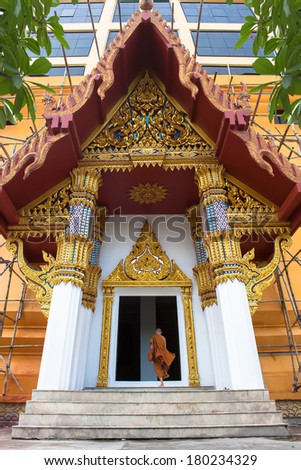 Buddhist monk going to pray in the big holy pagoda. He pass the beautiful gates with Thai definition art. Although it was repaired.