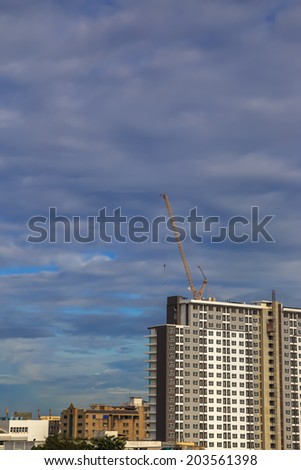 A yellow high construction crane has building condo or apartment in sunny day and rain could.