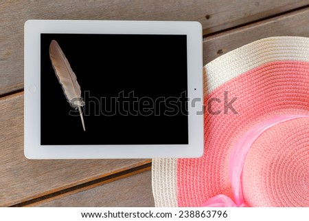 Tablet white frame and black screen  with feather and Beautiful woman\'s hat on wooden floor in  summer theme