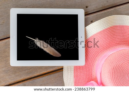Tablet white frame and black screen  with feather and Beautiful woman's hat on wooden floor in  summer theme