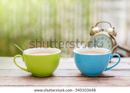 couple twin Coffee cup with spoon and alarm clock put on wooden floor with gren blur background and copy space