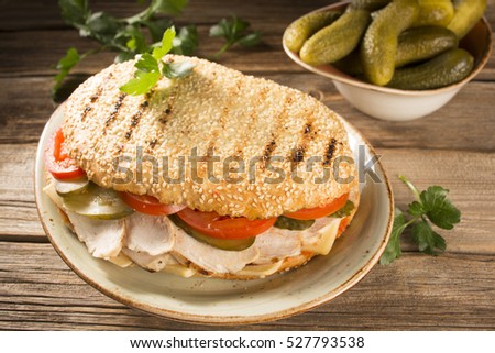 Crispy tomato, pickle, ham and cheese sandwich on a decorative plate with pickles and a piece of salad in the background