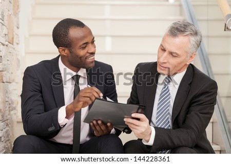 Two Businesspeople Sitting On Stairs And Looking At Papers.